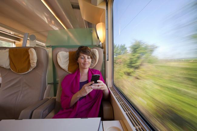 A woman on a train sat next to a window looking at her mobile device